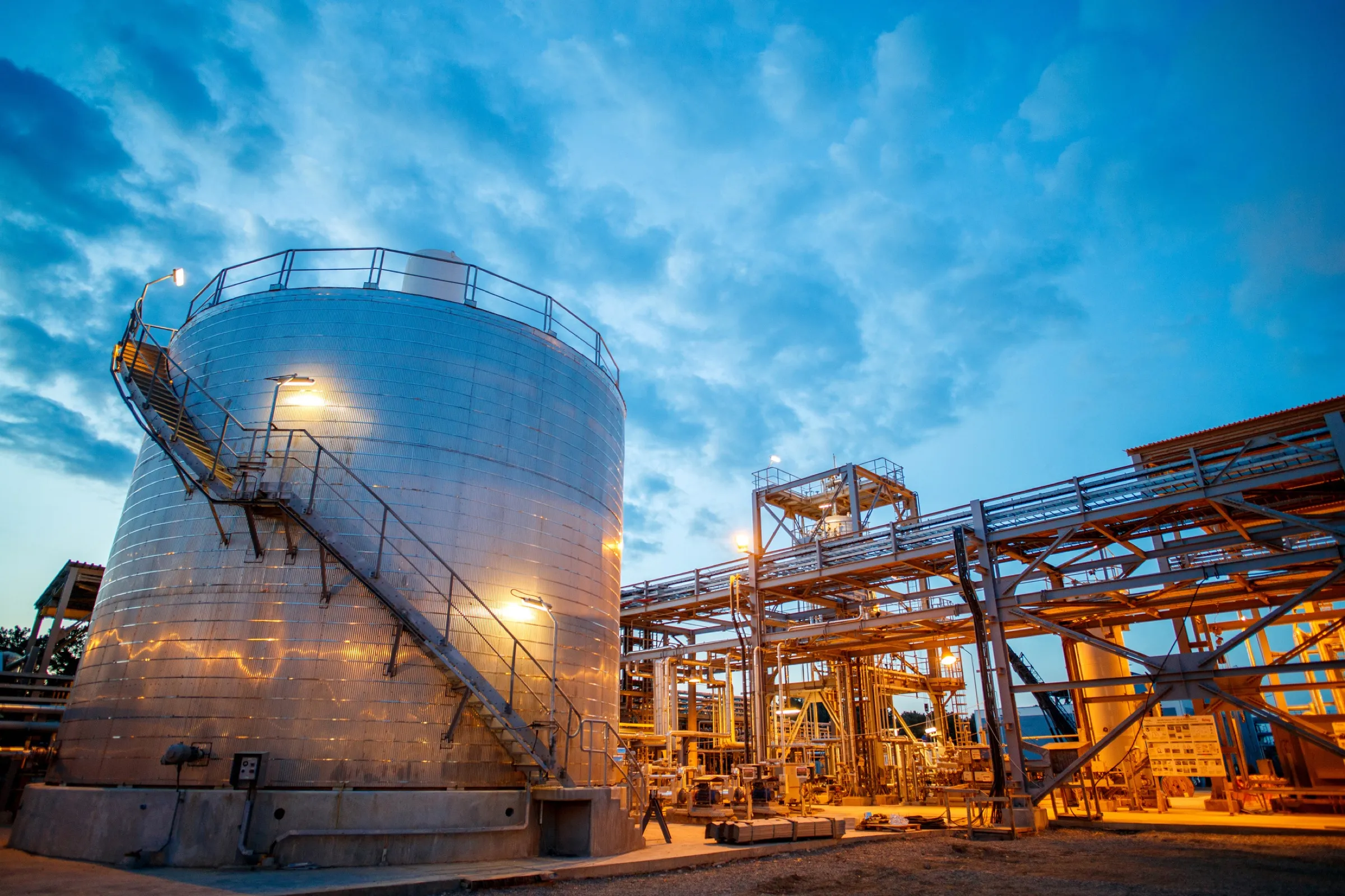 Tanque de almacenamiento y estructura de proceso al anochecer